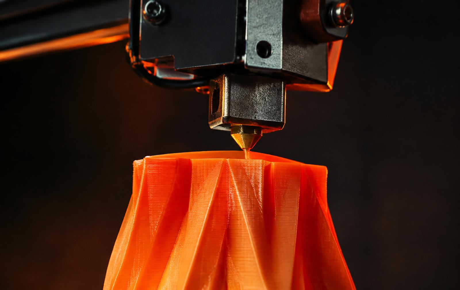 3D printer nozzle extruding orange filament